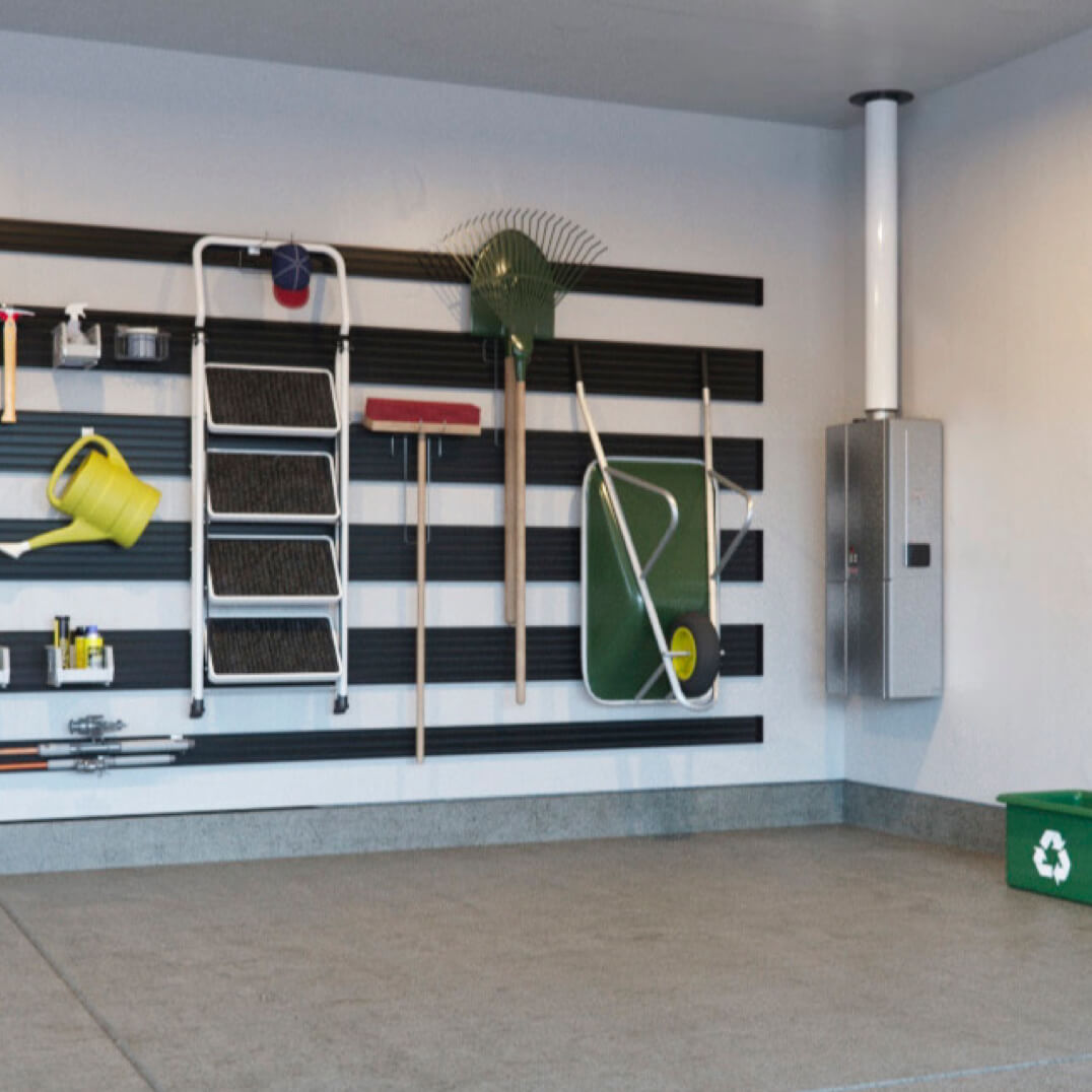 Lawn tools handing in garage next to wall mounted tankless water heater